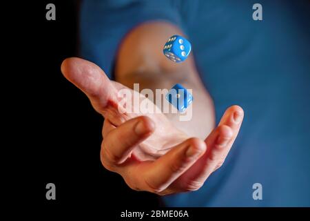 Main mâle caucasienne jetant des dés bleus dans l'air - gros plan avec peu de focus Banque D'Images
