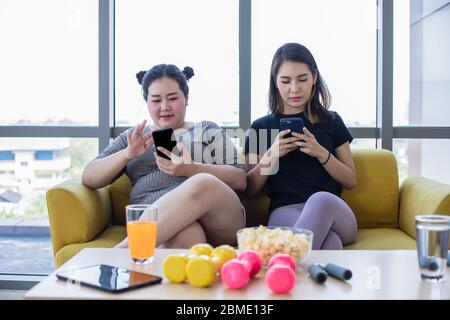 femme asiatique en surpoids avec un ami jouer au téléphone mobile et profiter de manger de la nourriture et du pop-corn sur le canapé à la maison Banque D'Images