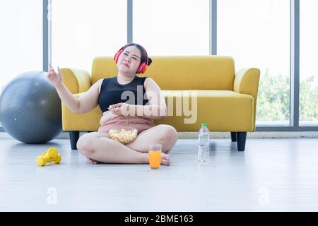 Femme asiatique en surpoids utilisant une tablette et. Port de casque pour écouter de la musique et elle s'exerce à la maison, fille asiatique aiment manger de la nourriture et du pop-corn Banque D'Images