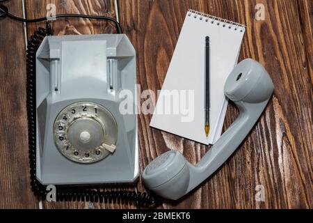 téléphone gris vintage, bloc-notes sur fond en bois, vue du dessus. Banque D'Images