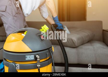 L'homme de l'aspirateur enlève la saleté des meubles dans plat, fermé, aspirateur nettoyer le canapé avec un équipement professionnel Banque D'Images