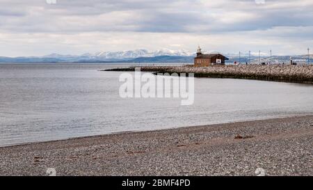 Morecambe, Angleterre, Royaume-Uni - 2 avril 2013 : le soleil illumine les montagnes enneigées du Lake District derrière la jetée de pierre de Morecambe dans le nord de l'Angleterre. Banque D'Images