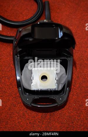 Un aspirateur avec un jeu de brosses et de sacs. Un aspirateur sur le tapis rouge. Banque D'Images