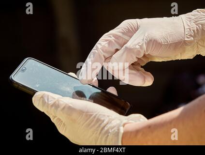 Personne utilisant un téléphone portable tout en portant des gants médicaux jetables, appelés EPI Banque D'Images