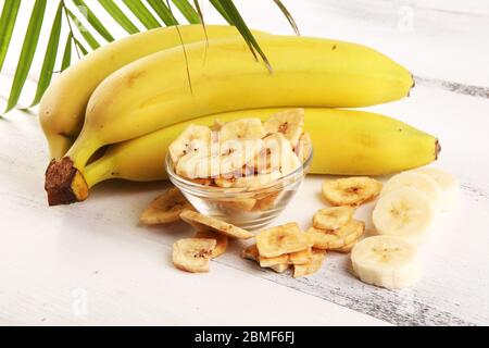 Croustilles de banane déshydratées faites maison dans un bol et bananes fraîches et tranches sur une table Banque D'Images