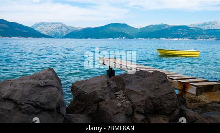 Côte rocheuse avec jetée en bois vers de belles montagnes et la mer avec un bateau jaune sur elle Banque D'Images