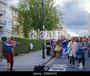 Street bucker joue le violon tandis que les acheteurs marchent le long du marché de Portobello. Notting Hill, West London, Angleterre, Royaume-Uni Banque D'Images