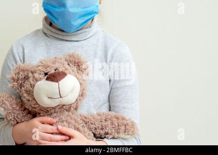 L'enfant tient l'ours en peluche portant un masque médical de protection sur fond blanc. Concept de soins de santé et de protection contre les virus. Banque D'Images