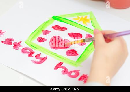 Gros plan de main de l'enfant dessin coeur à l'intérieur de la maison séjour à la maison mots par brosse avec aquarelles sur le papier blanc à la maison. Banque D'Images