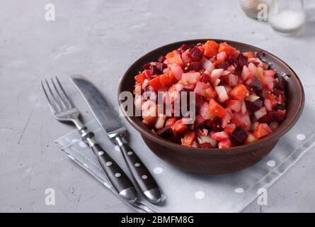 Vinaigrette traditionnelle russe à salade avec betteraves, carottes, pommes de terre et oignons dans un bol en argile sur fond de béton gris, nourriture végétarienne Banque D'Images