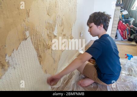 Un enfant aide à enlever le vieux papier peint d'un mur comme la première étape de la redécoration d'une chambre. Banque D'Images