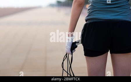 Femme tenant une corde de saut portant des gants de protection en latex chirurgical pour un entraînement sûr à l'extérieur Banque D'Images