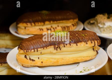 Dessert français traditionnel. Délicieux eclalairs avec crème anglaise et glaçage au chocolat pour les dents sucrées sur une assiette. Produits de pâtisserie. Banque D'Images