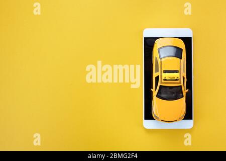 Voiture de taxi jaune jouet et smartphone sur fond jaune avec espace de copie. Vue de dessus Banque D'Images