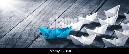 Blue Paper Boat diriger UNE flotte de petits bateaux blancs avec icône de boussole sur une table en bois avec lumière du soleil - concept de leadership Banque D'Images