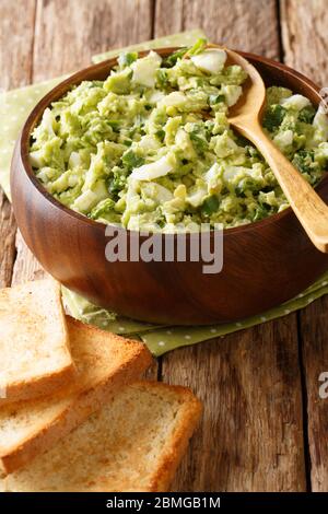 Salade d'avocat frais écrasée avec des œufs durs et des oignons verts dans un bol en gros plan sur la table. Verticale Banque D'Images