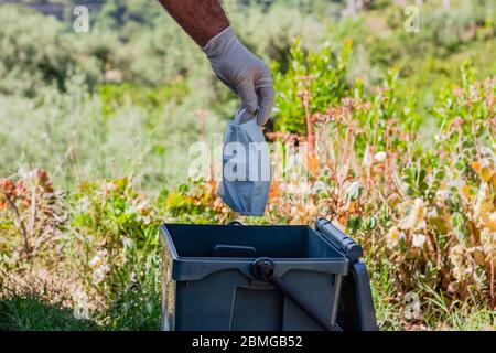 Homme jetant le masque chirurgical utilisé dans le bac de recyclage. Problème d'élimination des déchets à l'époque du coronavirus, Covid-19. Banque D'Images