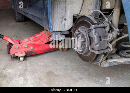 Remplacement des roues sur une voiture, le cric maintient la carrosserie en position relevée. Voiture sans roue et se soulever par hydraulique, en attendant le remplacement des pneus. Banque D'Images