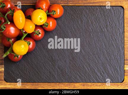 Tomates cerises fraîches rouges et jaunes sur un tableau noir en ardoise avec espace pour le texte Banque D'Images