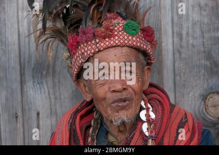 Banaue, Philippines - février 2012 : homme aîné en vêtements traditionnels assis devant un mur en bois Banque D'Images
