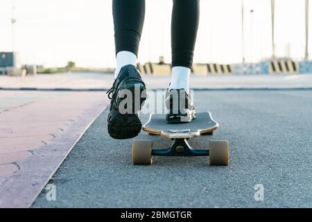 Une femme méconnue se déplace à bord d'une longboard autour d'un parc éclairé par le soleil. Banque D'Images