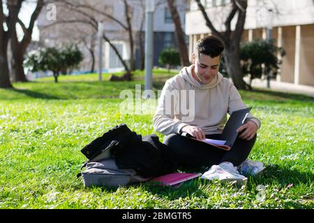 Adolescent assis sur l'herbe de l'école tout en étudiant avec un livre Banque D'Images