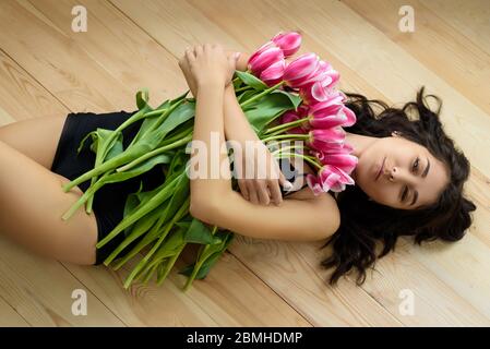 Un portrait de charmante jeune femme aux cheveux foncés avec beaucoup de belles tulipes roses sur le plancher en bois. Banque D'Images