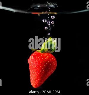Une fraise rouge fraîche qui est tombée dans l'eau avec des bulles d'eau et une éclaboussure d'eau Banque D'Images