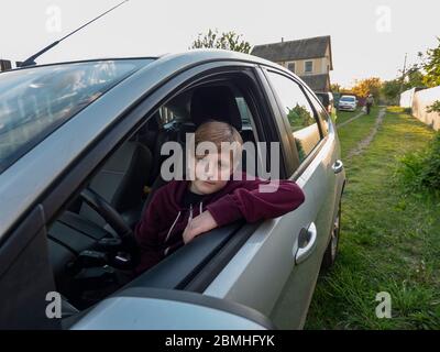 Un garçon caucasien de 11 ans est assis sur le siège du conducteur avant un voyage d'étude sous la direction de son père Banque D'Images