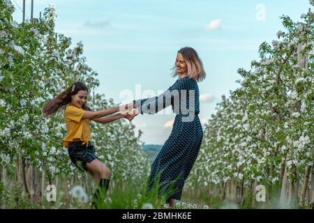 Mère tenant les mains de la petite fille et marchant heureusement autour de jardin fleuri Banque D'Images