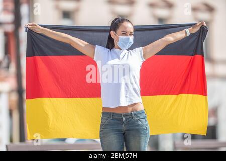 Une femme portant un masque facial porte un drapeau de l'Allemagne derrière elle. Banque D'Images