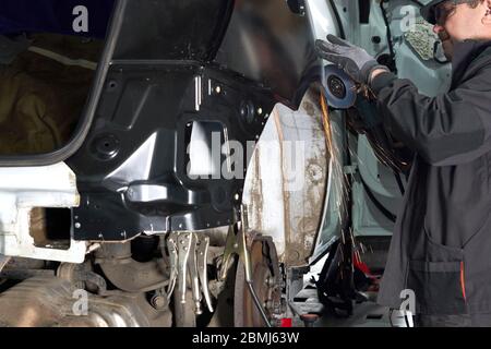 Le technicien de réparation répare la voiture endommagée. Utilisation d'une meuleuse d'angle pour fixer le corps en métal. Banque D'Images