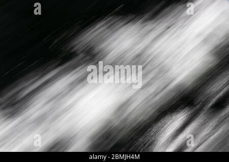 Image noir et blanc floue de l'eau en mouvement rapide mise en évidence par la lumière du soleil, évoquant la sensation de mouvement et de vitesse Banque D'Images