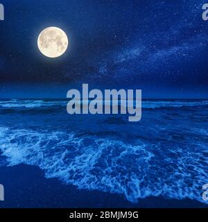 plage et mer par une nuit nuageux. vue magnifique sur les vagues qui roulent la côte sous un ciel lumineux, sous une pleine lumière de lune Banque D'Images