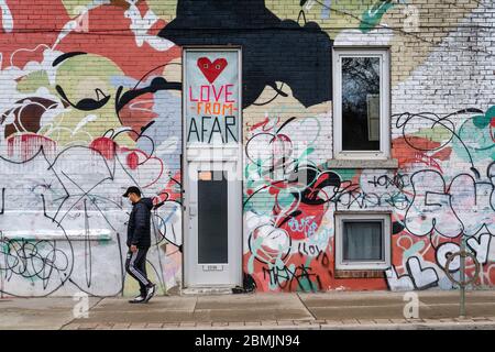 Toronto, Canada, un homme local portant un masque de marche devant un mur coloré présentant des signes sociaux de distanciation pendant une pandémie de coronavirus. Banque D'Images