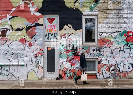 Toronto, Canada, un homme local portant un masque facial marche devant un mur coloré avec un message de distanciation sociale positif pendant une pandémie de coronavirus. Banque D'Images