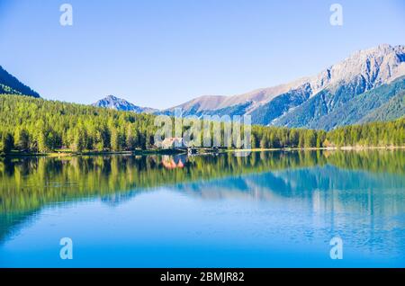 lac de montagne avec des eaux bleu pur, cabane agricole et bois vert sous un ciel clair Banque D'Images