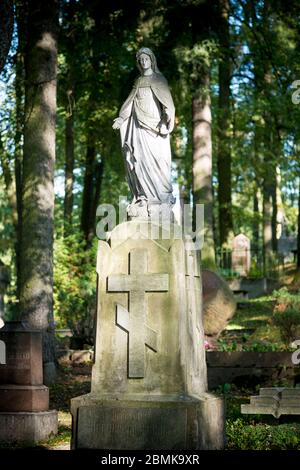 Une statue de la Vierge Marie sur une tombe avec une croix orthodoxe russe. Au cimetière d'Antakalnis à Vilnius, Lituanie. Banque D'Images