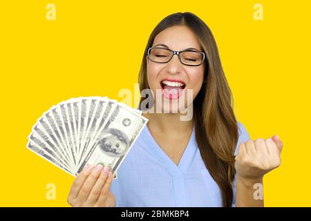 Portrait de la belle jeune femme qui rit et tient des billets de banque en dollars isolés sur fond jaune en studio. Concept de prêts faciles. Banque D'Images