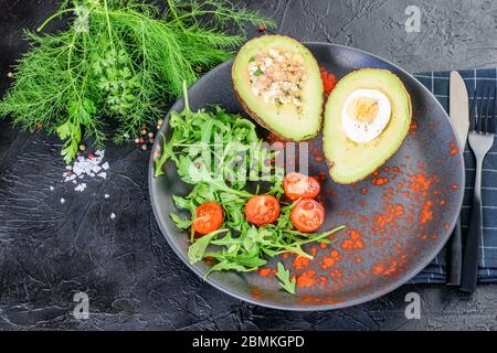 Avocat farci d'œufs, thon et sauce, tomates et légumes frais. Nourriture saine de Keto. Banque D'Images