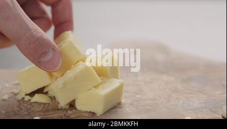 la main de l'homme prend le cube de fromage cheddar du bois d'olive gros plan Banque D'Images