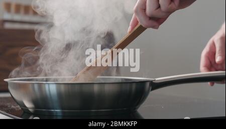 homme à la main en déplaçant quelque chose avec une spatule en bois dans un poêle à frire Banque D'Images