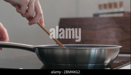 homme à la main en déplaçant quelque chose avec une spatule en bois dans un poêle à frire Banque D'Images