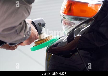 Homme utilisant un polisseur pour polir la carrosserie noire de la voiture dans l'atelier Banque D'Images
