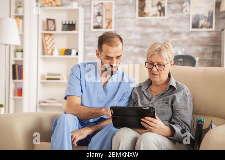 Un homme a été barbu médecin dans une maison de soins infirmiers aidant la femme à utiliser sa tablette. Banque D'Images