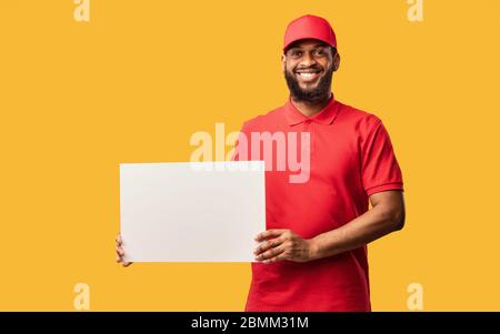 Un homme de livraison africain montrant une affiche blanche vide, un fond jaune, une maquette Banque D'Images