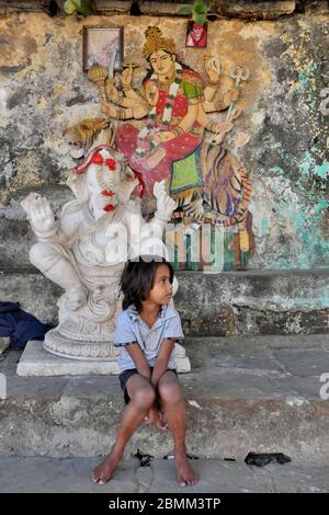 Une jeune fille est assise près d'une statue blanche de Ganesh, une fresque de la déesse Durga sur un tigre et un portrait de Shirdi Sai Baba en b/g ; Banganga Tank, Mumbai, Inde Banque D'Images