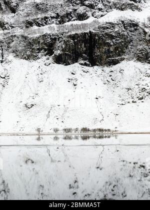 Isolated stand of trees at foot of snow covered mountain reflected in partially frozen river near Glencoe Scotland Banque D'Images