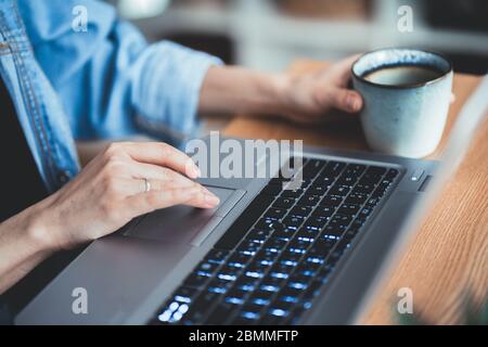 gros plan main de fille tenant le gobelet à café. Femmes d'affaires dactylographiant et défilement clavier sur ordinateur portable. Technologie femme concept de bureau Banque D'Images