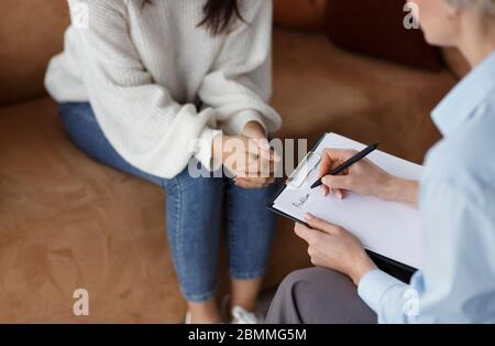 Psychologue méconnaissable parlant avec le client prenant des notes assis au bureau Banque D'Images